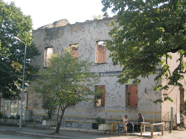 Life goes on: Men converse in front of bullet-holed building in Mostar