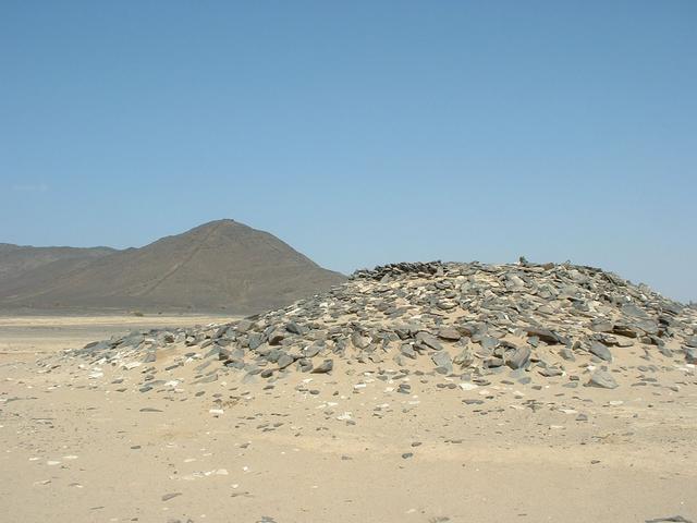 Cairn in front of a hill with long stone walls