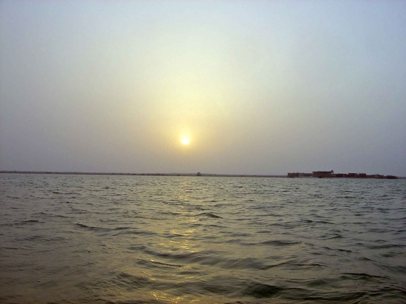 View of the confluence site, looking west towards the setting sun;  The shore and fenced-in beach camp dwellings are 288 m west of 26N 50E.