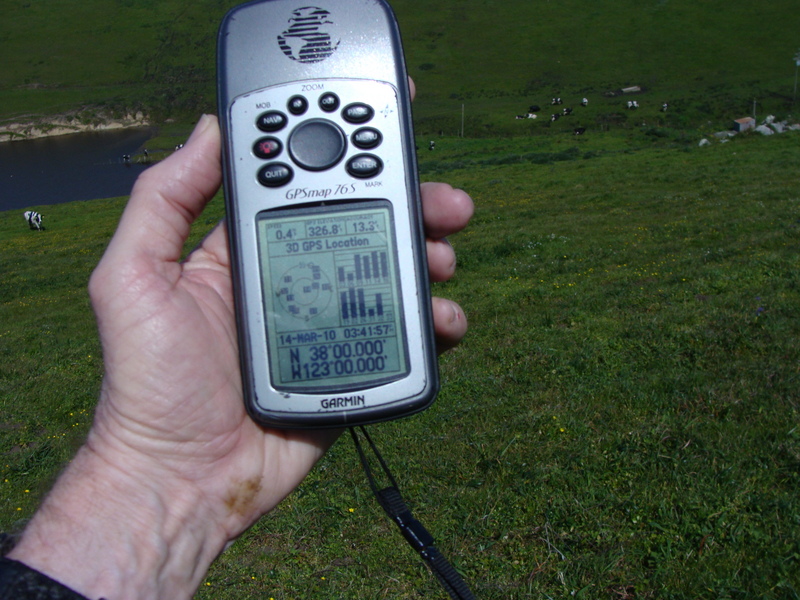 Hand holding GPS bears the marks of crawling throught the mud etc. under a barbed wire fence.