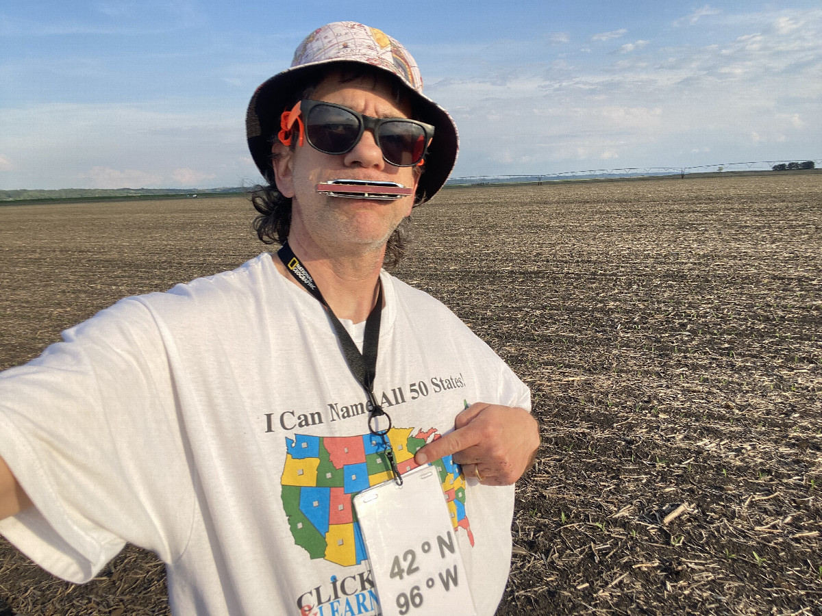 Joseph Kerski at the confluence point pointing at Iowa on his map shirt. 