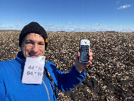 #9: Joseph Kerski at the confluence point, holding sign in teeth due to heavy winds. 