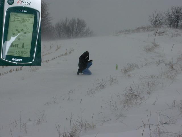 Tom kneels at the confluence while watching the GPS (inset).